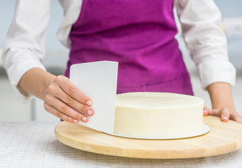 women's hands making biscuit cake with white cream  using a  cooking spatula