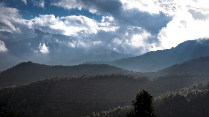 Mountain silhouettes on a cloudscape with rays of sun through the clouds