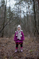 A little girl is standing in a forest on a path.