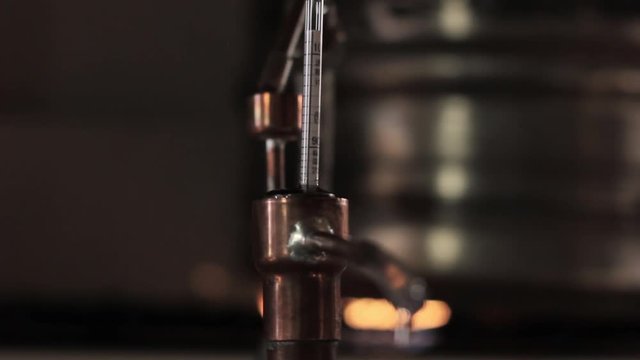 Home production of alcohol on flame fire. Alcohol distillation equipment, hooch fluid flow into glass jar