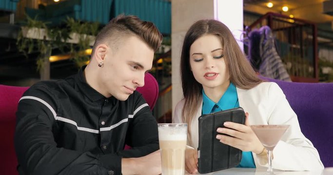 Modern young couple talking in cafe, looking together at tablet PC