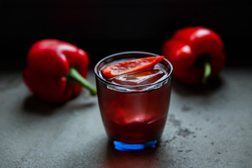 An underexposed horizontal image of an alcoholic drink, decorated with sweet red pepper, standing on a concrete surface. Selective focus.