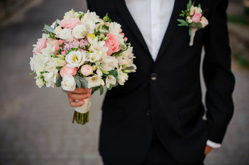 groom in a black suit with boutonniere holding a wedding bouquet