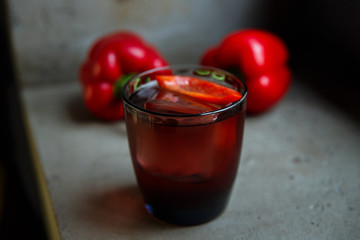 An underexposed horizontal image of an alcoholic drink, decorated with sweet red pepper, standing on a concrete surface. Selective focus.