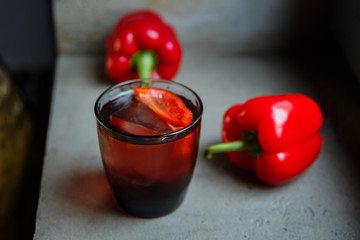 An underexposed horizontal image of an alcoholic drink, decorated with sweet red pepper, standing on a concrete surface. Selective focus.