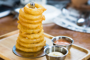 Delicious homemade appetizer. fried onion rings stack look like the tower serve with dip sauce on wooden tray.