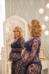 Fototapeta na wymiar beautiful woman in anticipation of a child looking in the mirror. Beautiful interior. Pregnant woman in blue lace
