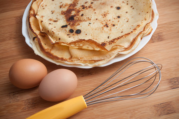 crêpes dans une assiette avec oeuf et fouet sur fond de planche à découper en bambou
