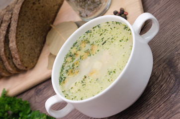 Mushroom soup with croutons in a white dish is on a wooden table.