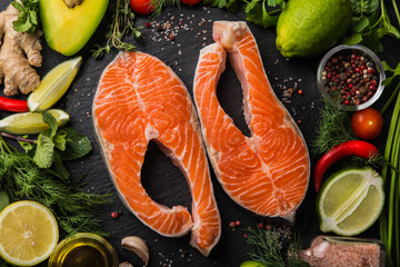 fresh raw salmon steaks with ingredients, spices and herbs on black background.