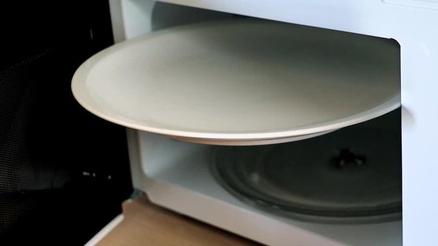 an open microwave with a white plate. An empty large disc is wedged in a microwave oven.