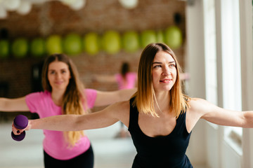 Happy two young women doing exercise with dumbbells in front of the window.