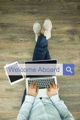 Young man sitting on floor with laptop and searching WELCOME ABOARD concept on screen