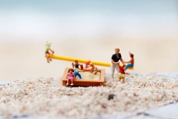 Obraz premium Miniature people: Children play on the swings on the beach with mother. Concept of happy family day.