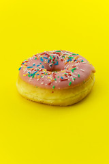 Close-up of a pink glazed donut isolated on yellow background. Strong candy contrast.