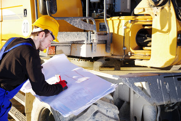 Mann in Arbeitskleidung auf einer Baustelle studiert Bau-Pläne 