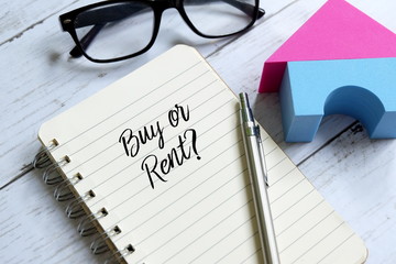 Sunglasses,home model,pen and notebook written 'BUY OR RENT?' on white wooden background.