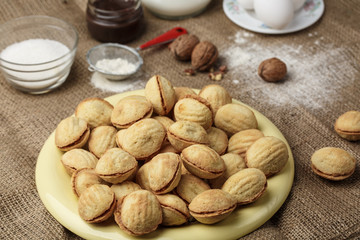 delicious walnut shaped shortbread sandwich cookies filled with sweet condensed milk and chopped pistachio nuts on brown clay dish. on old wooden background, view from above, close-up