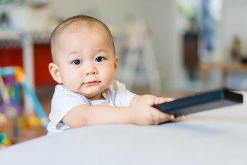 Happy smiling 10 month baby boy holding a remote control tv.child development concept.