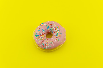Fototapeta na wymiar Close-up of a pink glazed donut isolated on yellow background. Strong candy contrast.