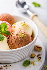 Set of ice cream scoops of different colors and flavours in white bowl with pistachio nuts and mint decoration. Summer food concept.