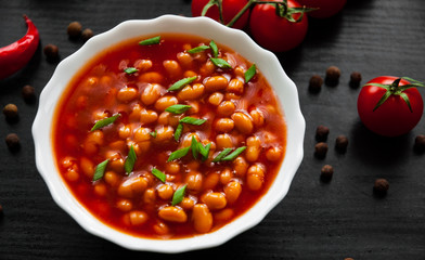 white beans in tomato sauce in a white bowl on dark wooden background
