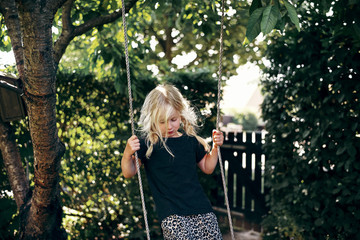 Cute little blonde girl playing on a tree swing outside