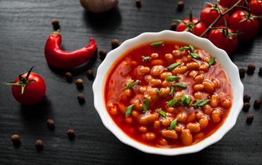 white beans in tomato sauce in a white bowl on dark wooden background