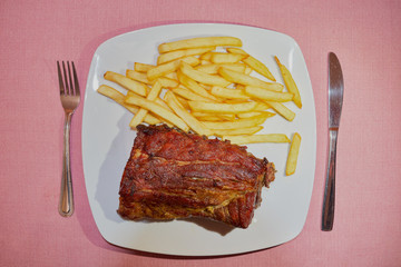 Rack of barbecued pork baby back ribs with french fries and dipping sauce and cutlery on tablecloth