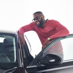 Feeling proud. Attractive young african man in stylish outfit standing near black luxury car model...