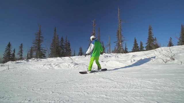 Sportsman drifts down on snowboard upon a slope of the mountain at sunny winter day