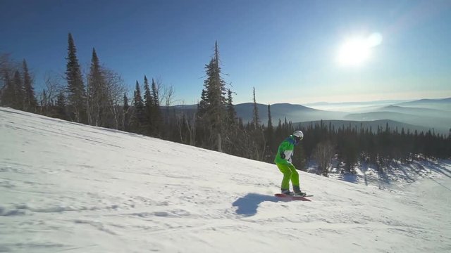 Sportsman drifts down on extreme snowboard upon a slope of the mountain at sunny winter day