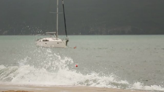 Storm on the sea. The wave breaks about the pier. Yacht in the background. Slow motion
