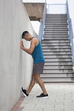 Young man stretching leg against wall