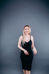 Beautiful woman with blond hair in the studio on a dark background in a black dress posing for us