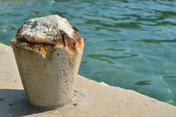 Old rusty concrete bollard for mooring boats on a mall with a sea in a background