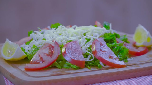 Delicious Grated Parmesan Cheese Salad ingredients with sliced arugula or rocket, tomato, lemon and parsley serving on bamboo cutting board rotating shot.