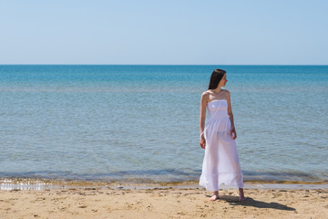 Fototapeta na wymiar A woman in a white dress walks on the beach