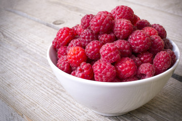 full bowl of juicy ripe raspberries, perfect colorful summer background with wood texture