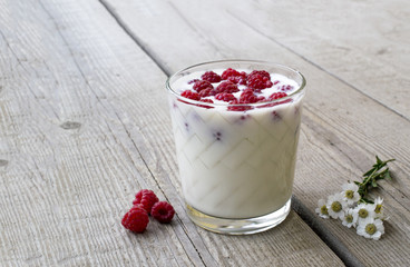 a glass with raspberries and milk, decorated with flowers on the background of a wooden table