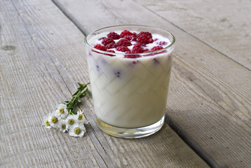 a glass with raspberries and milk, decorated with flowers on the background of a wooden table