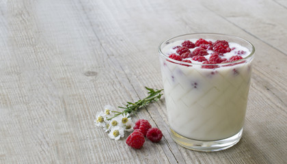 a glass with raspberries and milk, decorated with flowers on the background of a wooden table