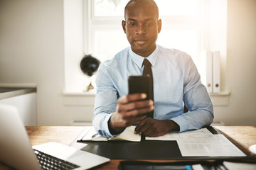 Businessman sitting at his desk reading messages on his cellphon