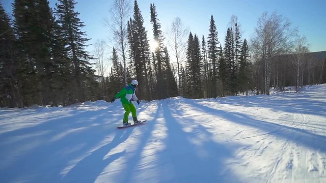 Sportsman is moving on extreme snowboard upon a slope of the mountain at winter sunny day