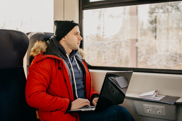 Man at the red jacket with the laptop going by train and watching at the window
