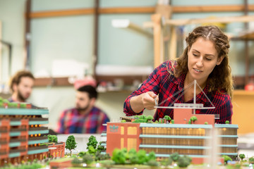 Female architect working over layout of new building on layout on background of two colleagues