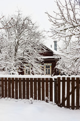 Village house under snow behind  wooden fence
