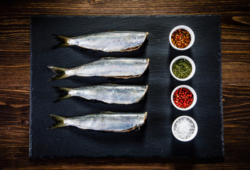 Fresh raw herrings with herbs served on black stone