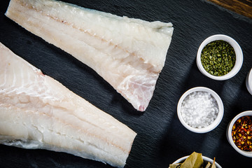 Fresh raw cod with herbs served on black stone on wooden table