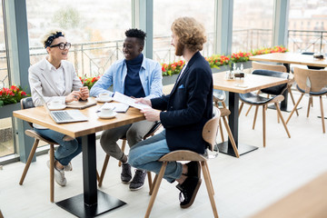 Small group of contemporary managers gathered by table in cafe to discuss new working ideas
